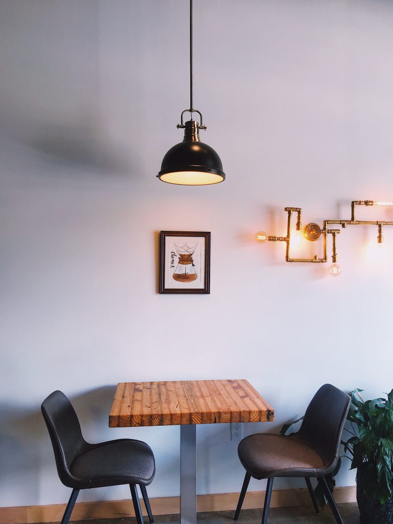 two industrial style dining chairs with a wooden table and exposed copper piping on the wall